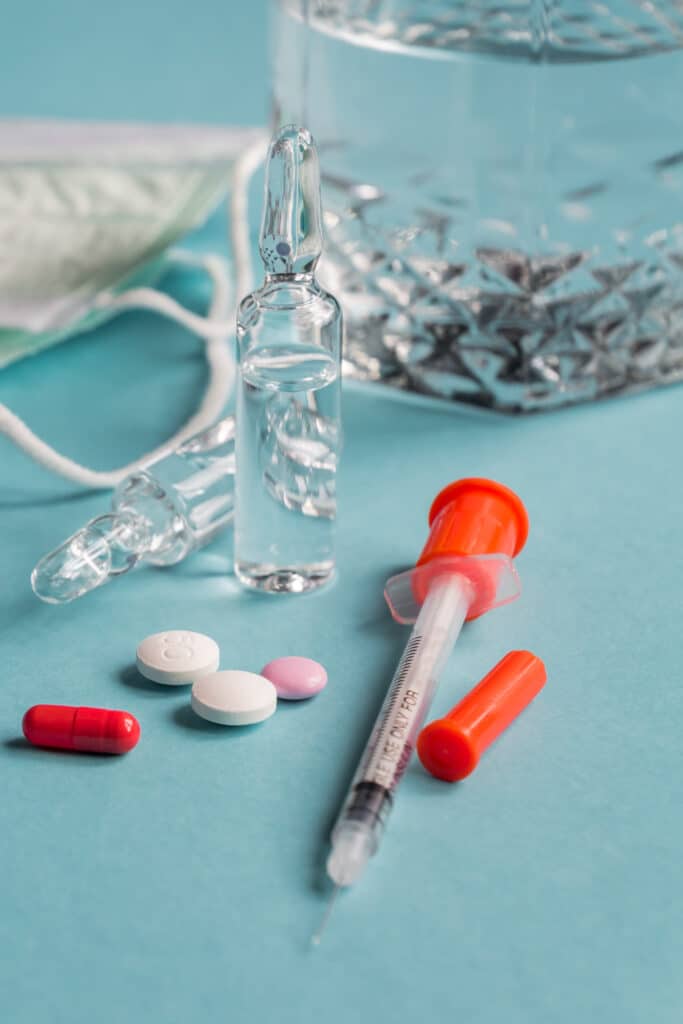 Close up of diabetes syringe with pills and glass vials on blue background. Healthcare concept